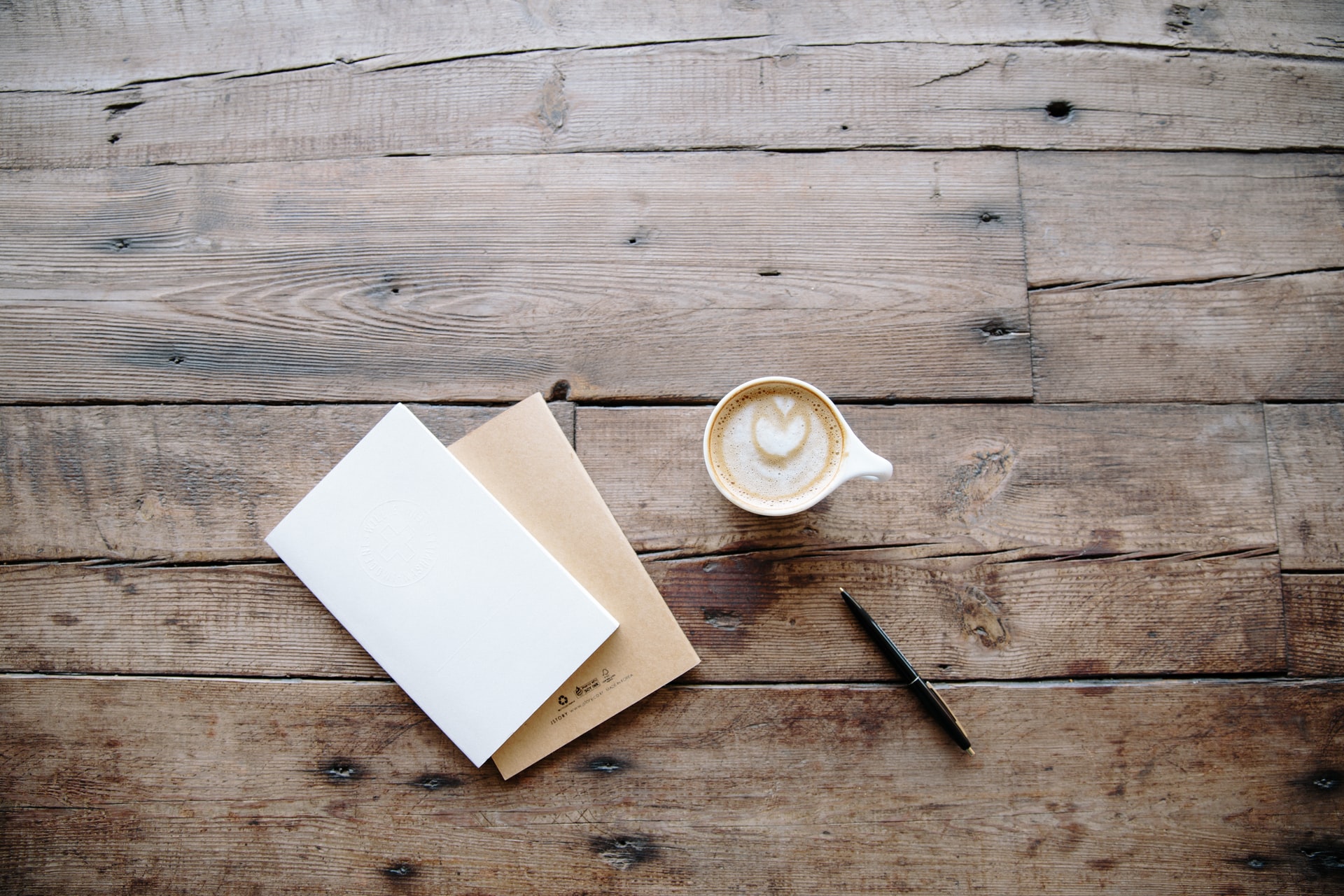 Coffee on a wooden table next to a pen and blank letter