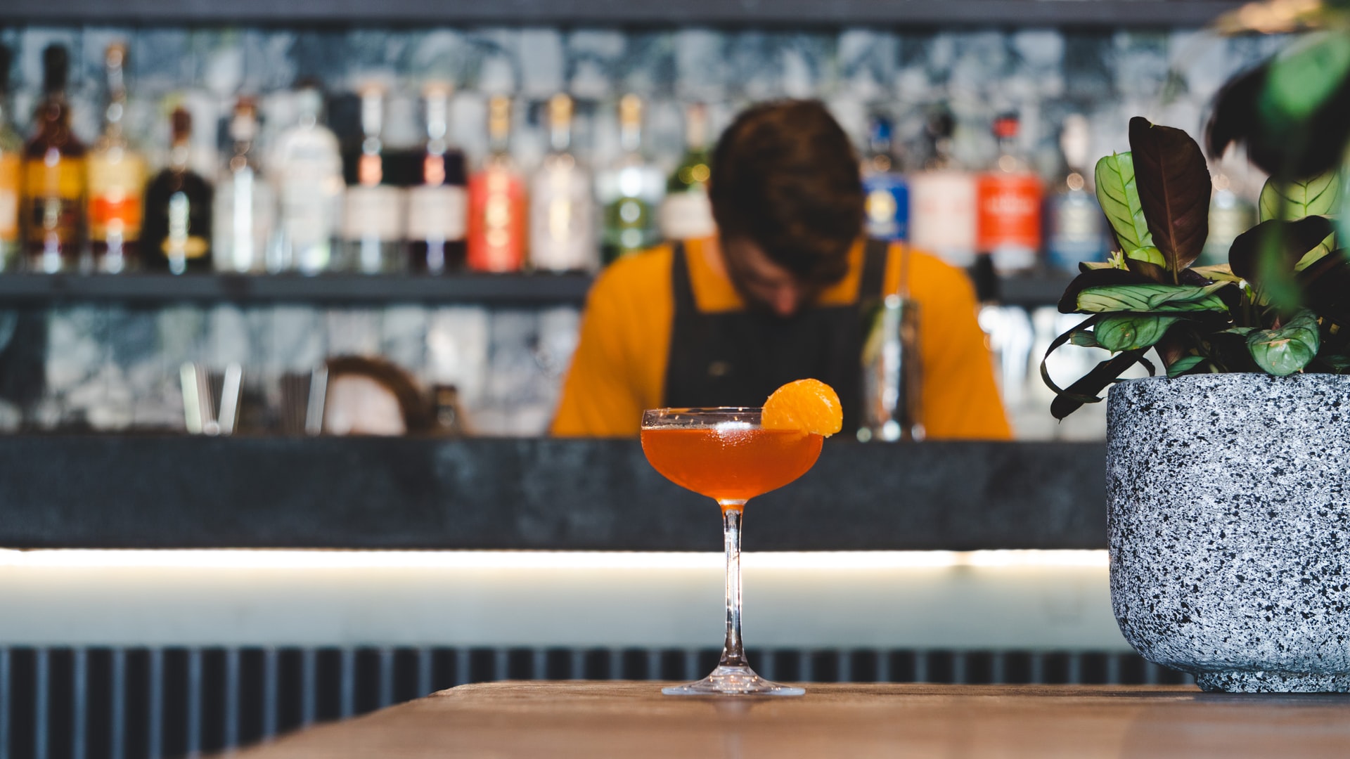 Bartender standing behind a drink with orange garnish